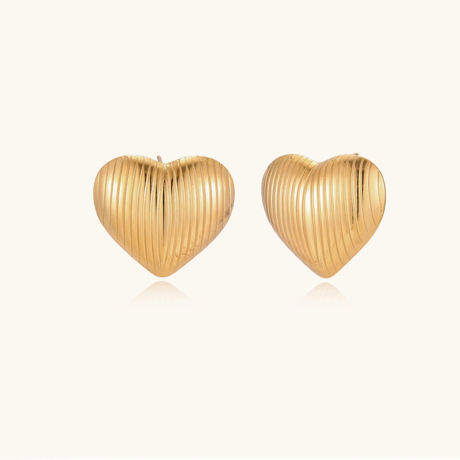 Gold-tone textured heart stud earrings on cream background