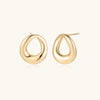 Gold-tone sculptural teardrop stud earrings on cream background