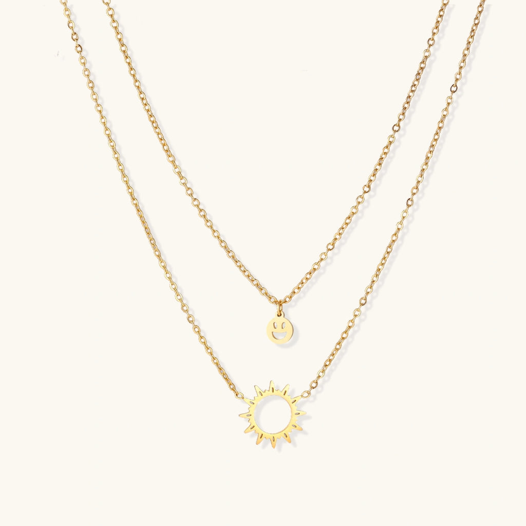 Gold-tone sun and smiley layered necklace on white background