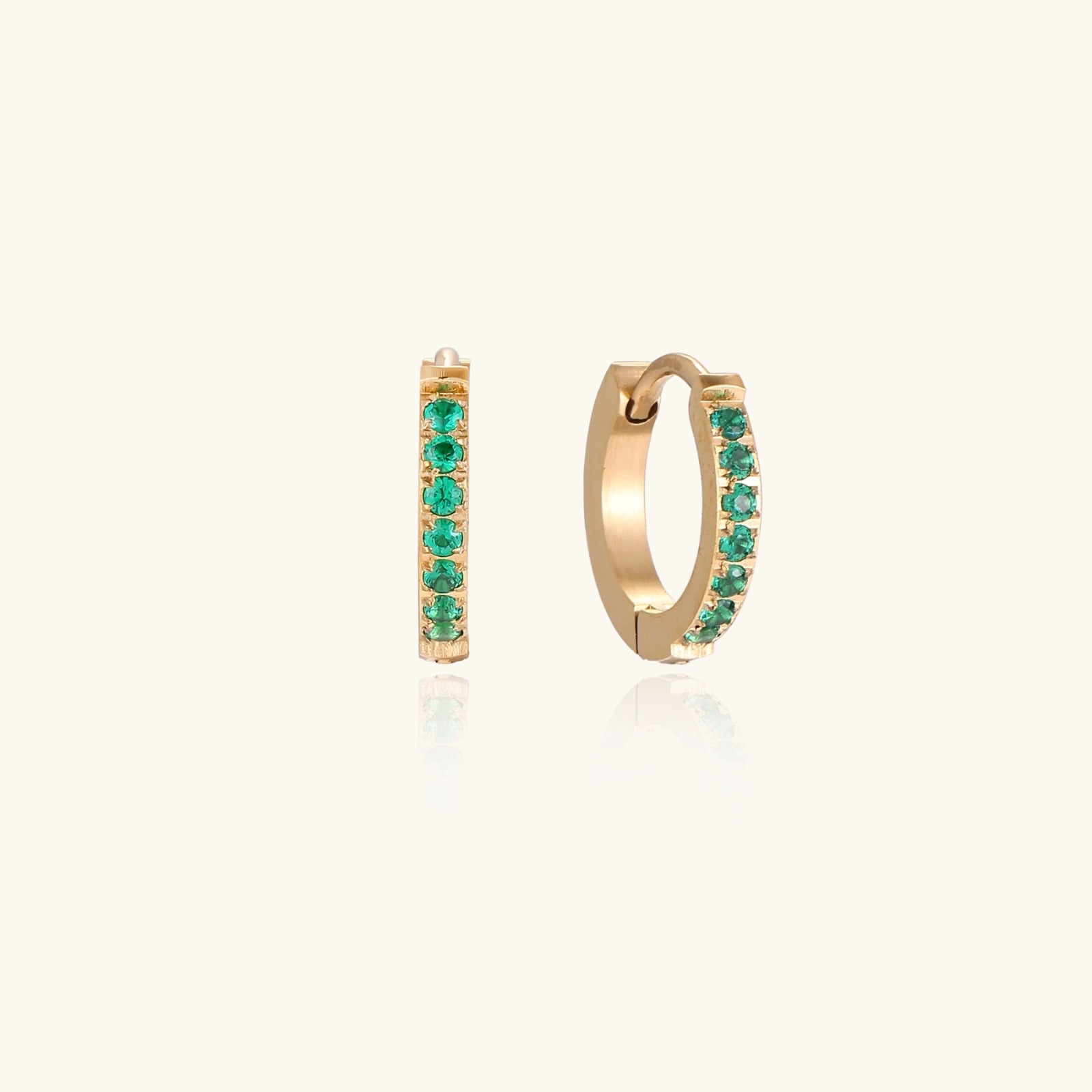 Emerald green CZ gold-tone huggie hoop earrings on cream background