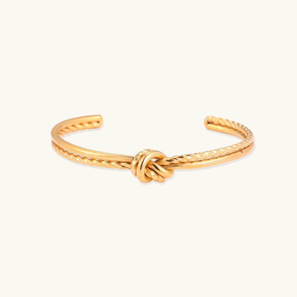 Gold-tone knot cuff bracelet with rope texture on cream background