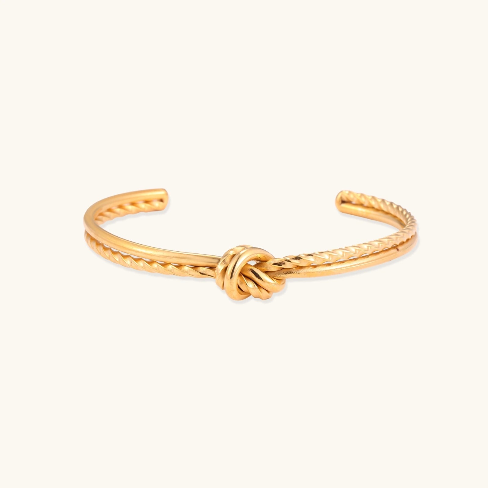 Gold-tone knot cuff bracelet with rope texture on cream background